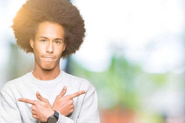 Fiatal afro-amerikai férfi afro hajú viselése sportos pulóver mutatva mindkét oldalán ujjal, eltérő irányba nem értenek egyet - Fotó, kép
