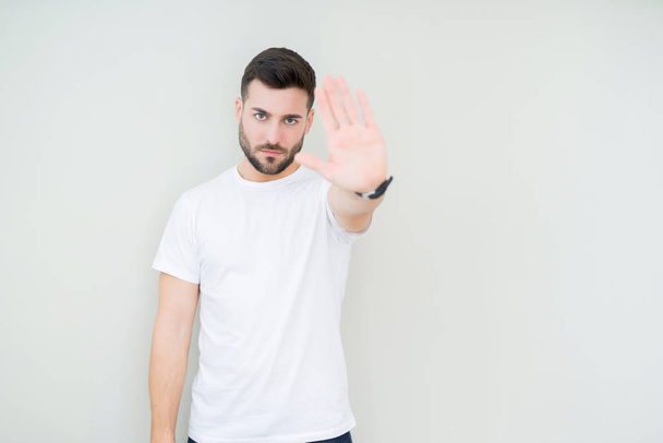 Young handsome man wearing casual white t-shirt over isolated background doing stop sing with palm of the hand. Warning expression with negative and serious gesture on the face. - Photo, Image