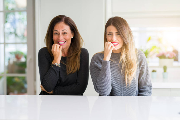 Beautiful family of mother and daughter together at home looking stressed and nervous with hands on mouth biting nails. Anxiety problem. - Photo, Image