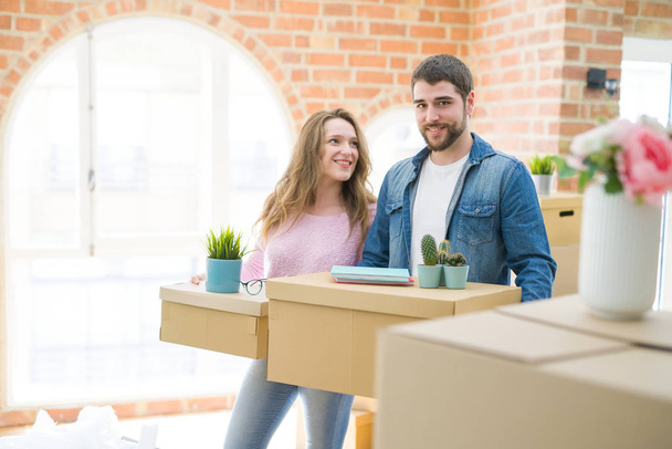 Jeune beau couple très heureux ensemble tenant des boîtes en carton déménageant dans une nouvelle maison
 - Photo, image