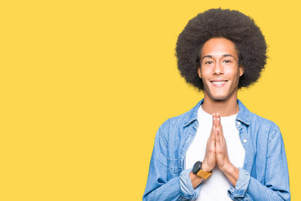 Молодий афроамериканець людиною з афро волосся молитися руками разом просити прощення посміхаючись впевнено. - Фото, зображення