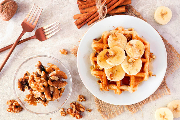 Breakfast waffle with bananas, walnuts and syrup. Top view table scene over a bright background. - Фото, зображення