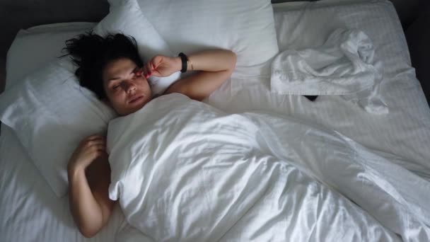 Top uitzicht jong vrouw wakker in bed onder deken. Schattig meisje controleert haar Smartphone eerste ding in de ochtend. - Video