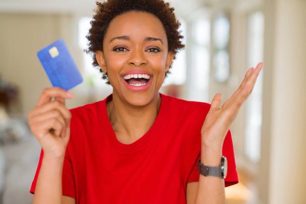 Молодая африканская американка держит кредитную карту очень счастливой и взволнованной, победитель выражение празднования победы кричал с большой улыбкой и поднял руки
 - Фото, изображение