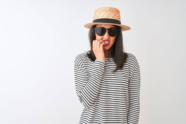 Chinese woman wearing striped t-shirt hat sunglasses standing over isolated white background looking stressed and nervous with hands on mouth biting nails. Anxiety problem. - Foto, imagen