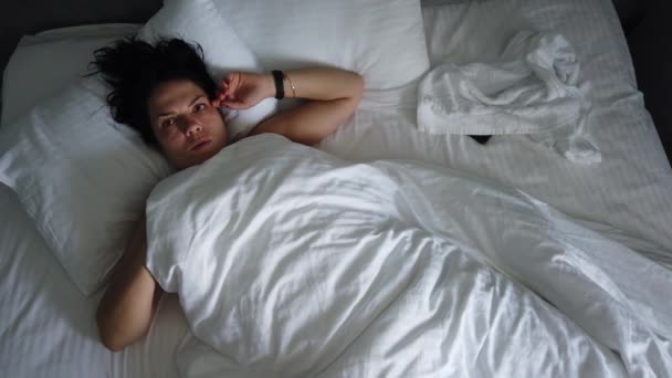 Vista dall'alto giovane femmina svegliarsi nel letto sotto coperta. Ragazza carina controlla il suo smartphone prima cosa al mattino
. - Filmati, video