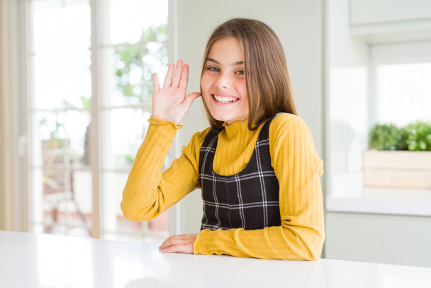 Jovem linda menina loira usando camisola amarela casual em casa Dispensa dizer olá feliz e sorridente, gesto de boas-vindas amigável
 - Foto, Imagem
