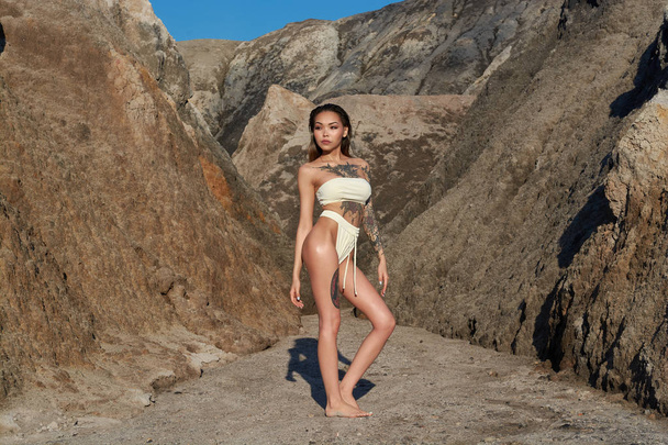 Asian girl with a tattoo stands in the mountains in a white bikini - Foto, Bild
