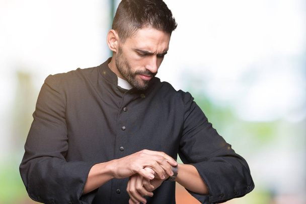 Jeune prêtre chrétien sur fond isolé Vérifier le temps sur la montre-bracelet, détendu et confiant
 - Photo, image