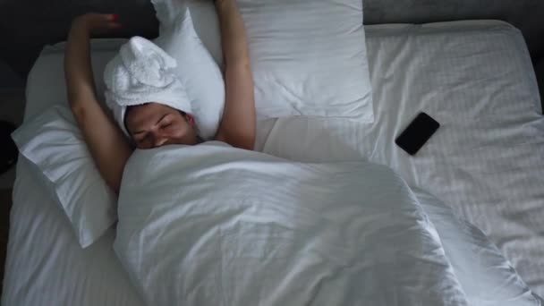 Top view young female waking up in bed under blanket. Cute girl checks her smartphone first thing in the morning. - Filmagem, Vídeo