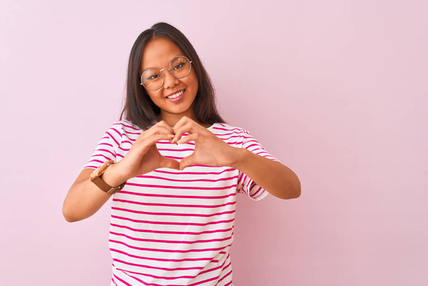 Young chinese woman wearing striped t-shirt and glasses over isolated pink background smiling in love doing heart symbol shape with hands. Romantic concept. - Foto, Imagem