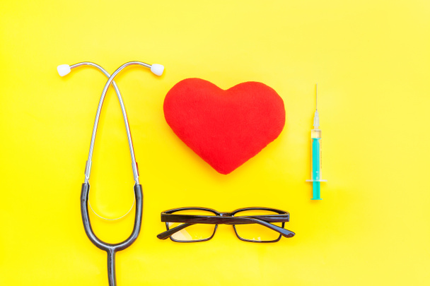 Medycyna sprzęt stetoskop lub fonendoskop okulary strzykawki i czerwone serce na białym tle na modne żółte tło - Zdjęcie, obraz