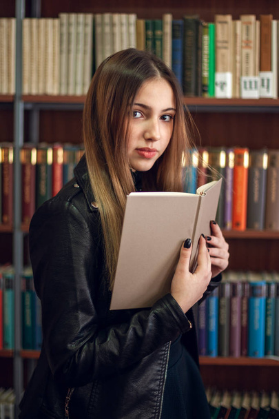 Beautiful teenager schoolgirl reading a book in the library - Photo, Image