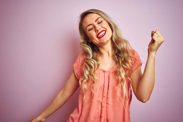 Jovem mulher bonita vestindo camiseta em pé sobre fundo isolado rosa Dançando feliz e alegre, sorrindo em movimento casual e confiante ouvir música
 - Foto, Imagem