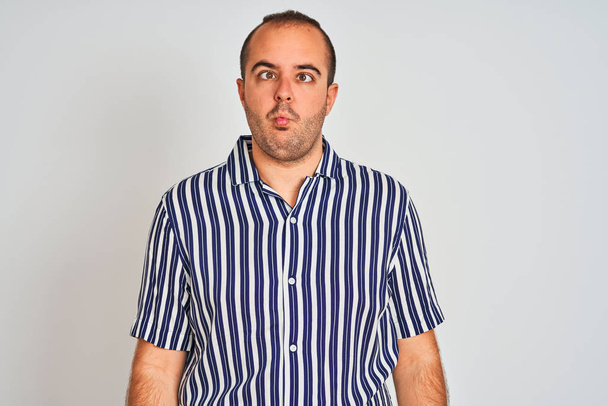 Young man wearing blue striped shirt standing over isolated white background making fish face with lips, crazy and comical gesture. Funny expression. - Photo, Image
