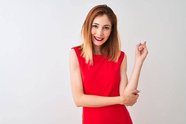Femme d'affaires rousse portant une élégante robe rouge debout sur un fond blanc isolé avec un grand sourire sur le visage, pointant du doigt vers le côté en regardant la caméra
. - Photo, image