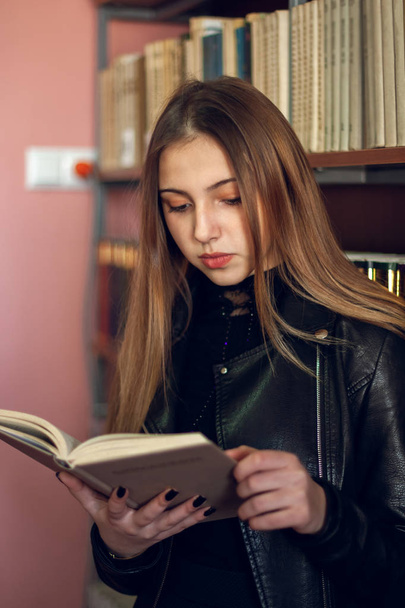Beautiful teenager schoolgirl reading a book in the library - Zdjęcie, obraz