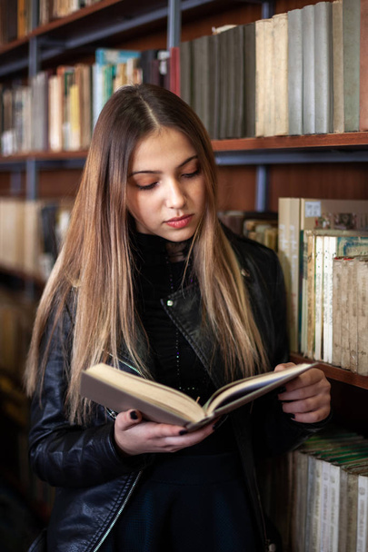 Beautiful teenager schoolgirl reading a book in the library - Fotó, kép