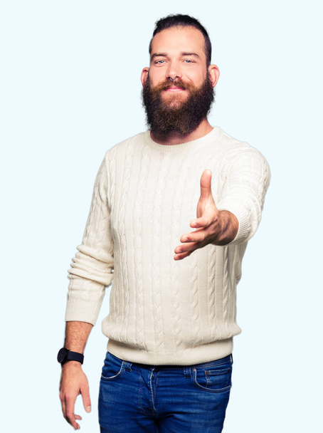 Jonge hipster man dragen winter trui lachende vriendelijke aanbod als begroeting en het welkom heten handdruk. Succesvol bedrijf. - Foto, afbeelding