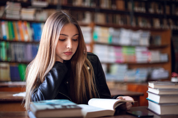 Belle écolière adolescente assise dans la bibliothèque et lisant
 - Photo, image