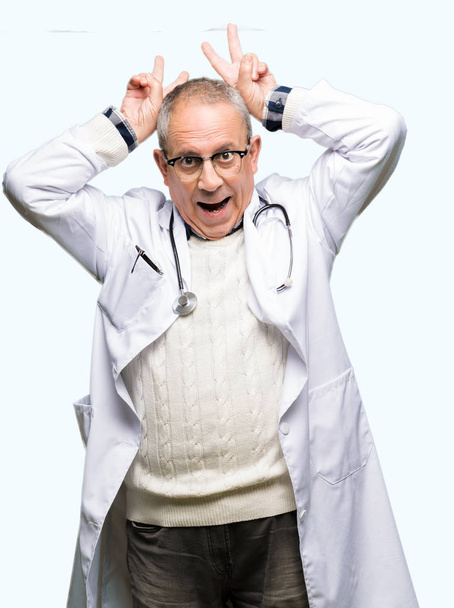 bello anziano medico uomo indossare medico cappotto posa divertente e pazzo con le dita sulla testa come coniglietto orecchie, sorridente allegro
 - Foto, immagini