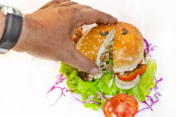 Um hambúrguer grande tamanho foi dividido em dois piolhos com uma mão
. - Foto, Imagem