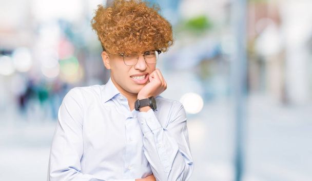 Nuori komea liikemies, jolla on afro-lasit, näyttää stressaantuneelta ja hermostuneelta kädet suulla pureen kynsiä. Ahdistuneisuusongelma
. - Valokuva, kuva