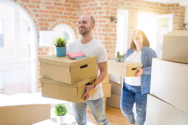 Jeune couple déménageant dans une nouvelle maison, souriant heureux tenant boîtes en carton
 - Photo, image