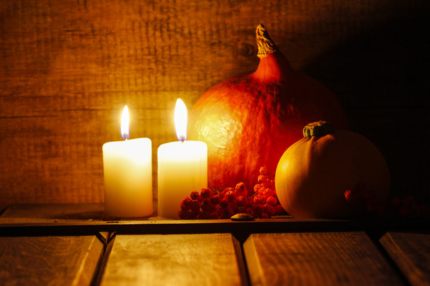 Two small candles burning in old wooden hut. Big orange pumpkin - Zdjęcie, obraz