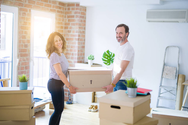 Middle age senior couple moving to a new house, holding cardboard boxing smiling happy in love with apartmant - Photo, image