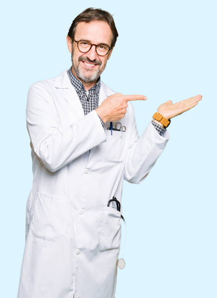 医療を着て中年医師男性コート驚かれるとカメラに笑みを浮かべて手を差し出しながら指で指しています。. - 写真・画像