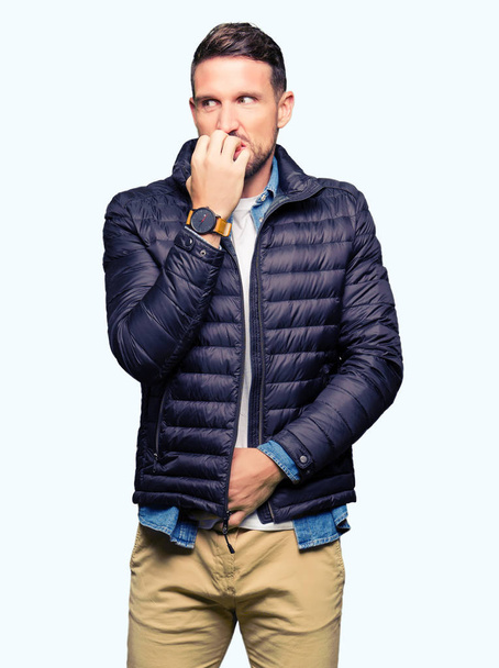 冬のコートを着たハンサムな男は、口を噛む爪に手を当て、ストレスと緊張を見ています。不安の問題. - 写真・画像
