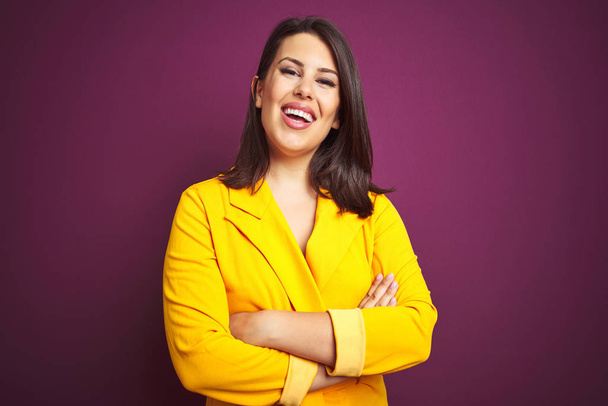 Young beautiful brunette woman wearing elegant yellow jacket over purple isolated background happy face smiling with crossed arms looking at the camera. Positive person. - Photo, Image
