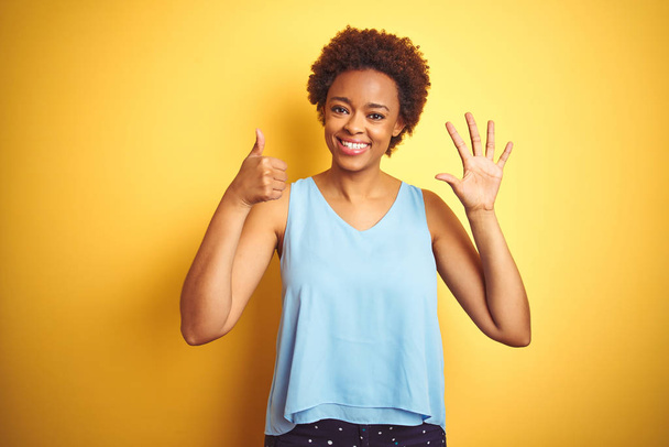 schöne afrikanisch-amerikanische Frau trägt elegantes Hemd über isoliertem gelben Hintergrund und zeigt mit Finger Nummer sechs nach oben, während sie selbstbewusst und glücklich lächelt. - Foto, Bild