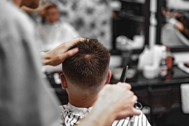 Men's haircut in a barbershop. Hairdresser cuts with scissors. - Foto, afbeelding