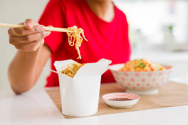 Close up of young woman eating noodles from delivery box using c - Photo, image
