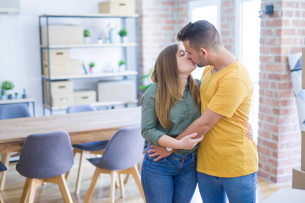 Νεαρό όμορφο ζευγάρι στην αγάπη γύρω από χαρτοκιβώτια που κινούνται σε νέο σπίτι, χαμογελαστά πολύ χαρούμενοι και χαρούμενοι για το νέο διαμέρισμα - Φωτογραφία, εικόνα