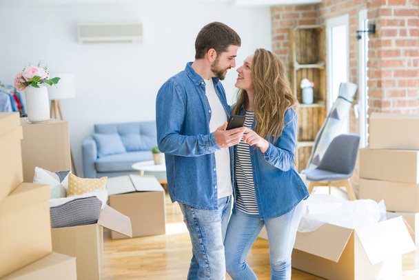 Young couple moving to a new house using smartphone around cardboard boxes - Photo, Image