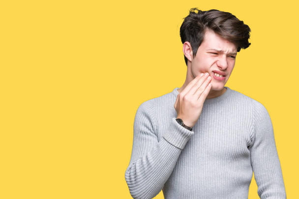 Молодой красивый мужчина в зимнем свитере на изолированном фоне касается рта рукой с болезненным выражением лица из-за зубной боли или зубной болезни на зубах. Концепция дантиста
. - Фото, изображение