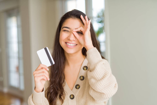 Young woman holding credit card as payment with happy face smiling doing ok sign with hand on eye looking through fingers - Zdjęcie, obraz