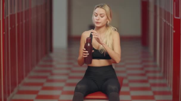 Vermoeide Sportvrouw opening sport fles in kleedkamer. Sexy meisje nippen water - Video