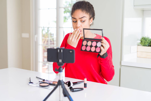 Jonge African American influencer vrouw opname make-up tutorial cover mond met de hand geschokt met schaamte voor fout, uitdrukking van angst, bang in stilte, geheime concept - Foto, afbeelding