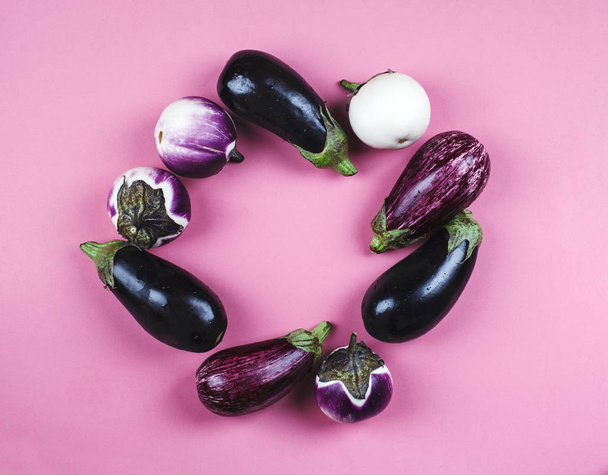 Fresh eggplants of different color and variety on a pink backgro - Фото, зображення