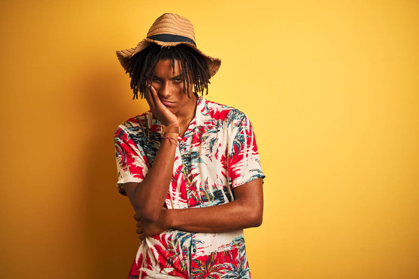 Afro american man with dreadlocks wearing floral shirt and hat over isolated yellow background thinking looking tired and bored with depression problems with crossed arms. - Fotoğraf, Görsel