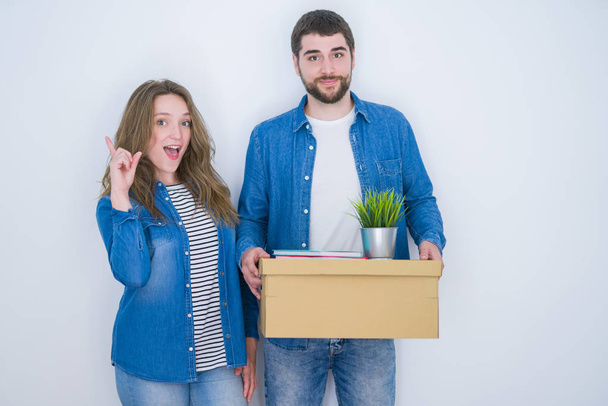 Young couple holding cardboard box moving to new house over white isolated background surprised with an idea or question pointing finger with happy face, number one - Φωτογραφία, εικόνα