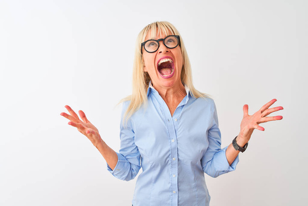 Middle age businesswoman wearing elegant shirt and glasses over isolated white background crazy and mad shouting and yelling with aggressive expression and arms raised. Frustration concept. - Valokuva, kuva