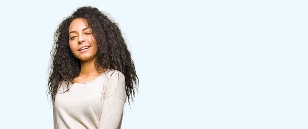 junge schöne Mädchen mit lockigem Haar trägt lässigen Pullover zwinkernd in die Kamera mit sexy Ausdruck, fröhliches und glückliches Gesicht. - Foto, Bild