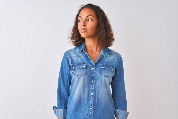 Young brazilian woman wearing denim shirt standing over isolated white background smiling looking to the side and staring away thinking. - Foto, Imagen