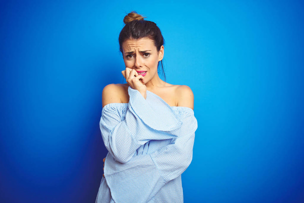 Young beautiful woman wearing bun hairstyle over blue isolated background looking stressed and nervous with hands on mouth biting nails. Anxiety problem. - Photo, Image