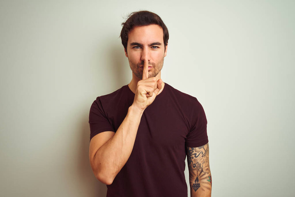 Young handsome man with tattoo wearing purple casual t-shirt over isolated white background asking to be quiet with finger on lips. Silence and secret concept. - Photo, Image